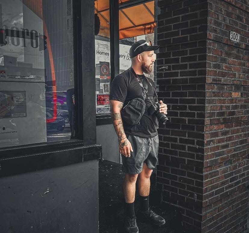 Portrait of Elijha Parks, photographer and owner of Elijha Parks Photography, standing in an urban storefront with a professional camera.