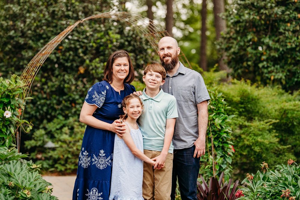 Family of four posing together in a lush garden with a decorative arch backdrop.