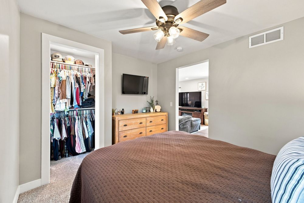 Bedroom with brown bedspread, ceiling fan, wood dresser, wall-mounted TV, and open walk-in closet with organized shelving.