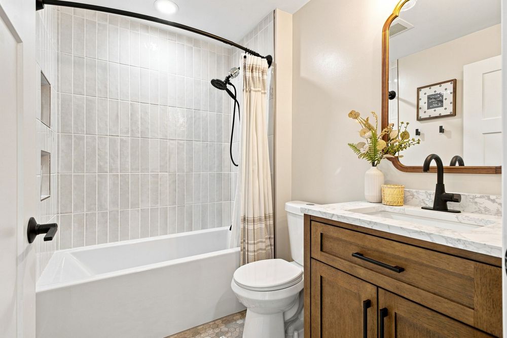 Modern farmhouse bathroom with wood vanity, marble countertop, white subway tile shower, and curved curtain rod.