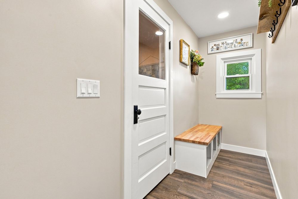 Bright mudroom entryway with white door, built-in bench, wood top, and hardwood floors in a modern home.