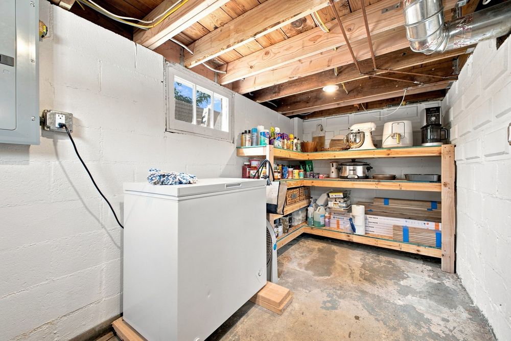 Unfinished basement laundry area with washer, wooden storage shelves, concrete floor, and exposed ceiling joists.