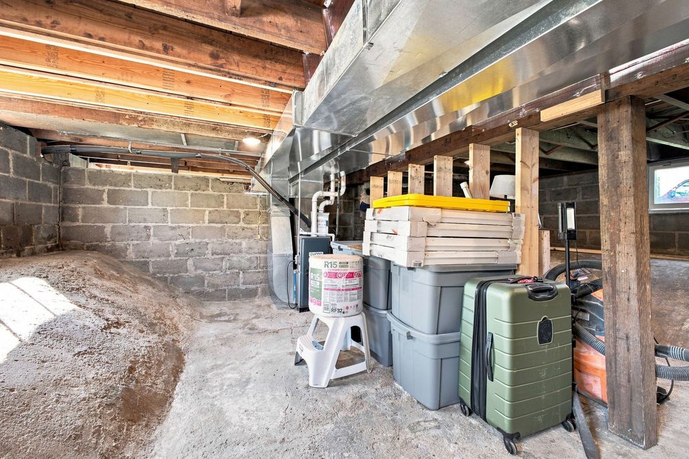 Unfinished basement storage area with concrete block walls, dirt floor, and various storage containers on wooden shelving.