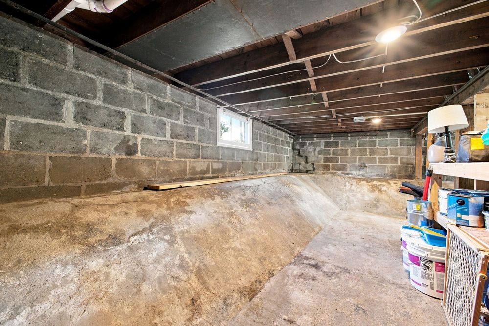 Unfinished basement with concrete block walls, exposed ceiling joists, and storage shelves with supplies.