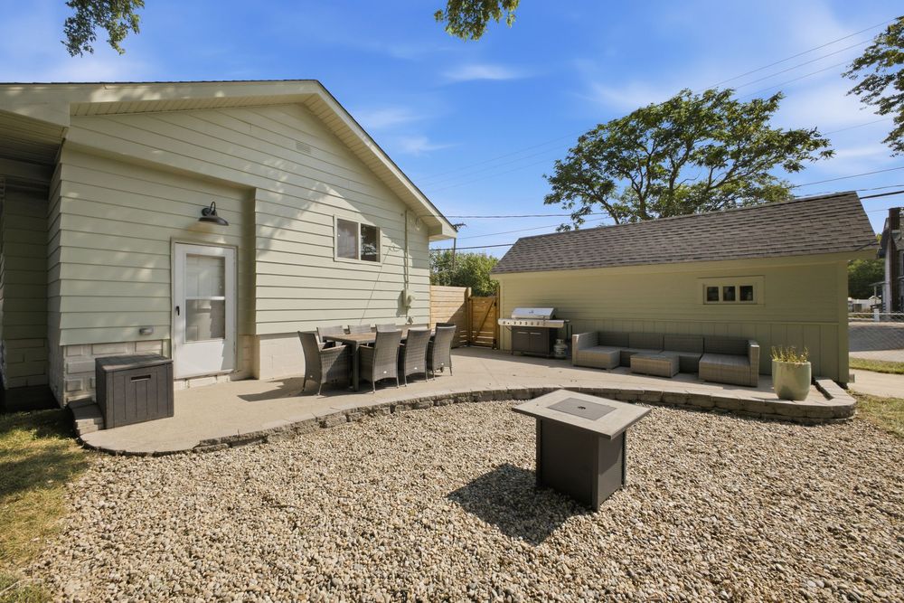 Backyard patio with gravel landscaping, outdoor seating, fire pit, and a detached garage surrounded by mature trees.