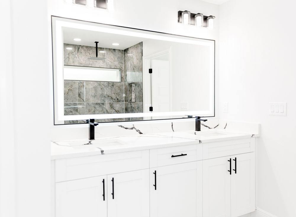 Modern double vanity bathroom with white cabinets, black hardware, LED mirror, and marble tile shower.