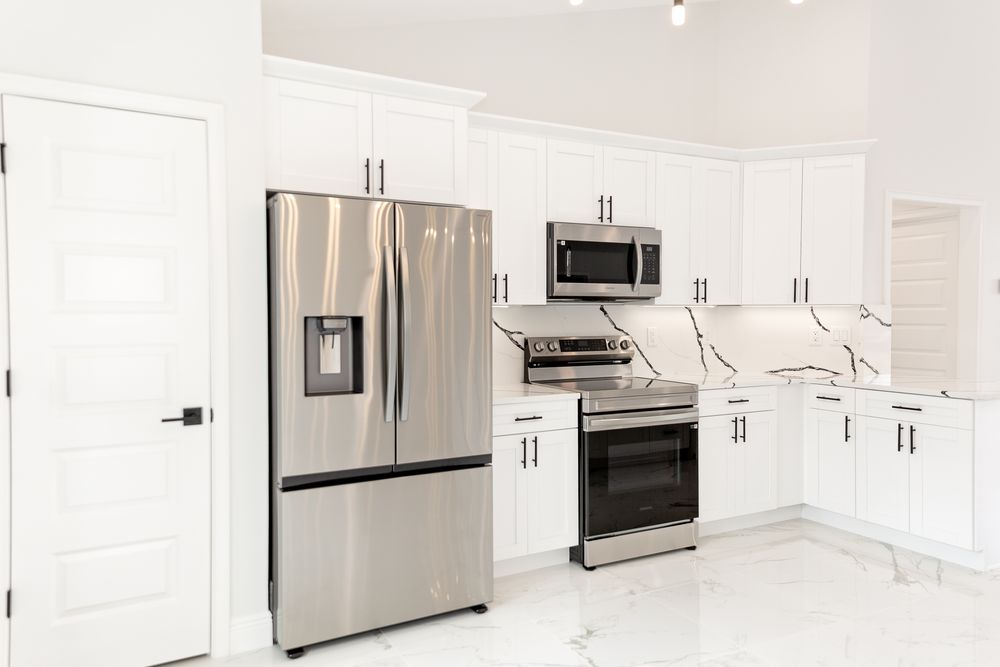 Modern kitchen with white cabinets, stainless steel refrigerator, microwave, and range on marble tile floors.