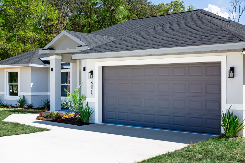 Modern white ranch-style home with dark gray garage door, manicured landscaping, and concrete driveway under clear skies.