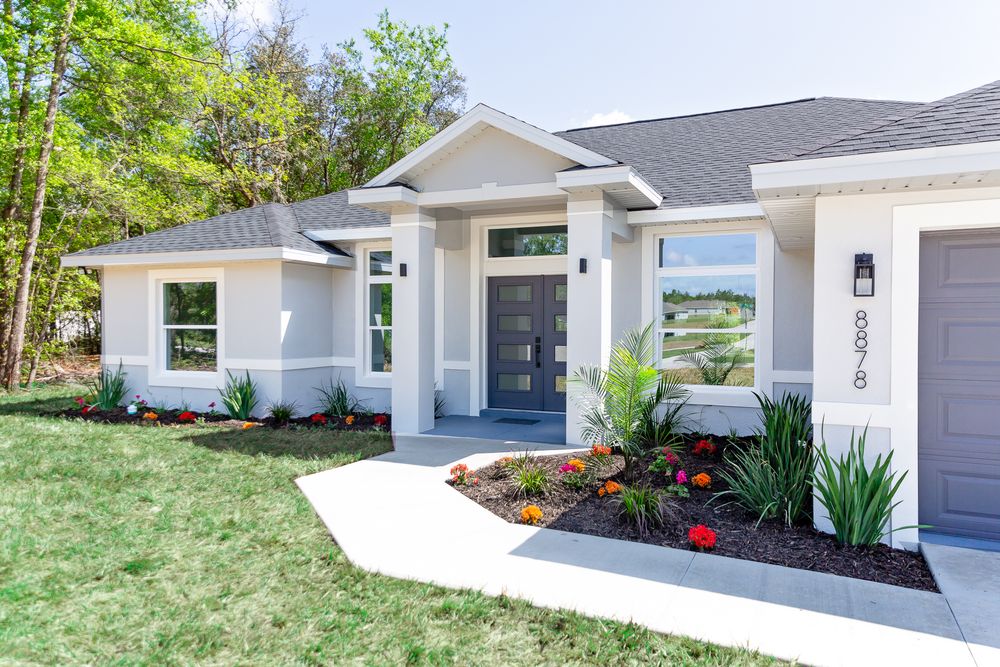 Modern single-story home with gray exterior, manicured landscaping, and elegant double front doors.