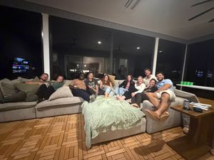 Group of friends relaxing together on large sectional sofa on covered patio at night.