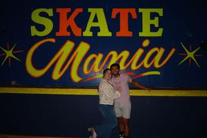 Couple posing together in front of a colorful Skate Mania sign at a roller skating rink.
