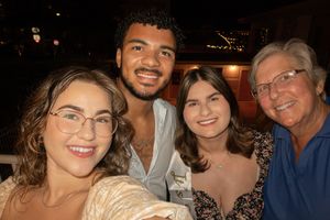 Four smiling friends pose together for a selfie at an outdoor evening gathering, capturing a joyful group moment.