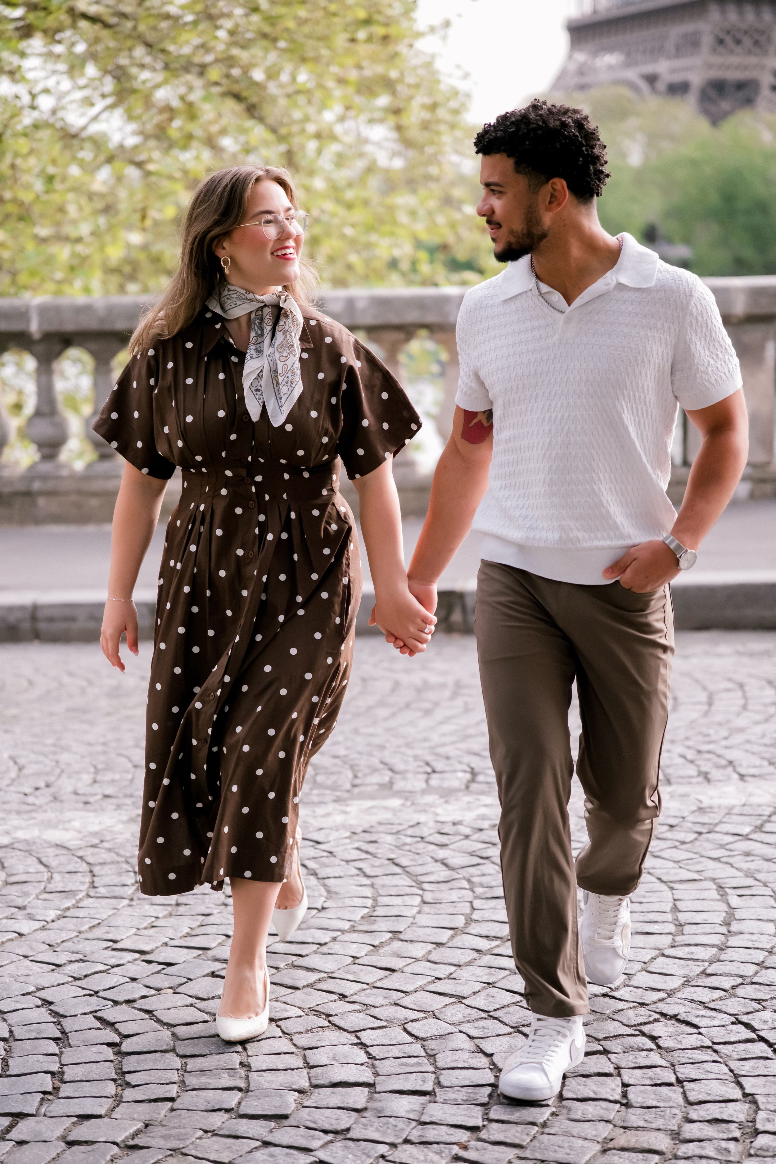 Couple walking hand in hand on cobblestone street near the Eiffel Tower in Paris.