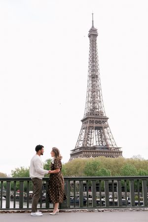 Couple holding hands on a bridge with the Eiffel Tower in Paris, France behind them.