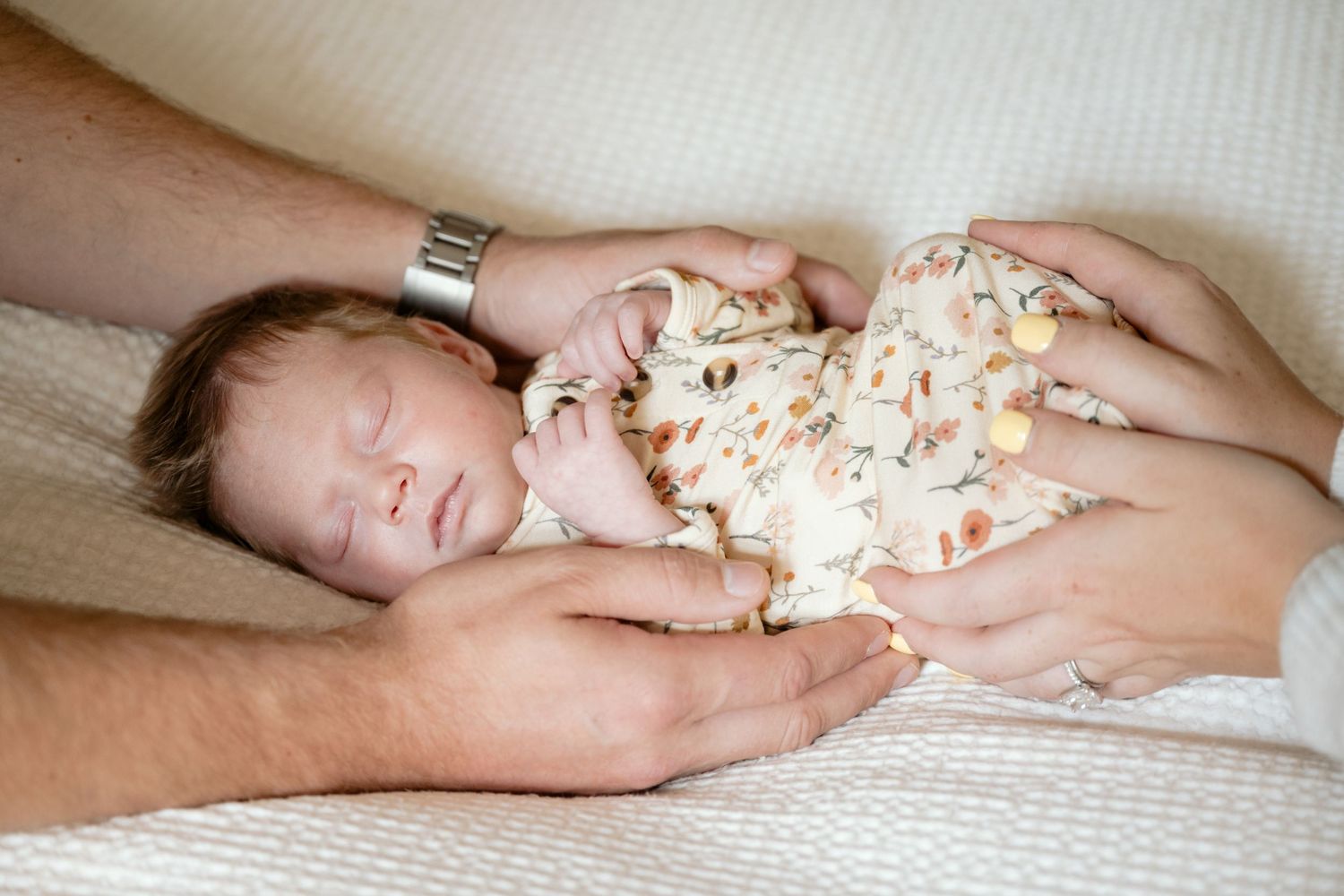 Full body portrait of sleeping newborn baby swaddled and being held by parents hands during in-home lifestyle newborn session in Minnetonka.