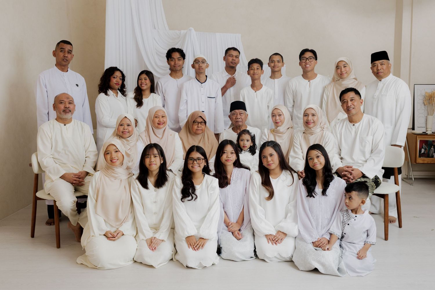 Large family group portrait in matching white outfits posing together in a bright studio setting.