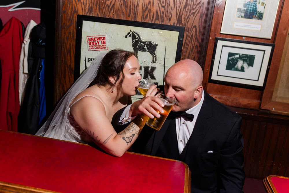 Bride and groom sharing a beer together at a pub on their wedding day, dressed in bridal gown and tuxedo.