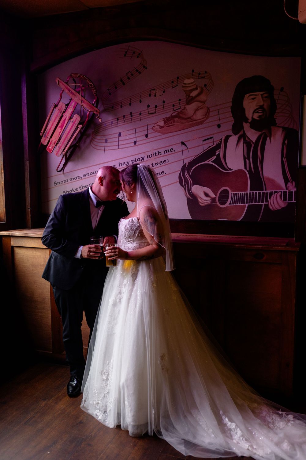 Bride and groom share a romantic moment at a music-themed bar, with a guitarist mural backdrop on their wedding day.