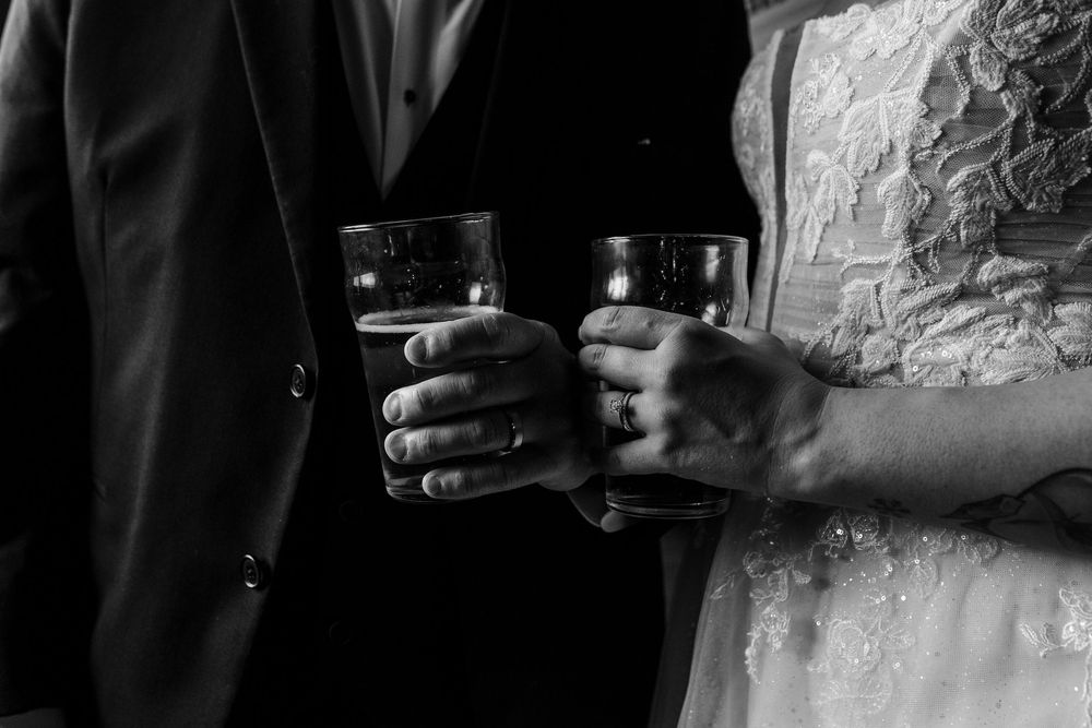 Black and white photo of bride and groom clinking glasses in a wedding toast, wearing formal attire.