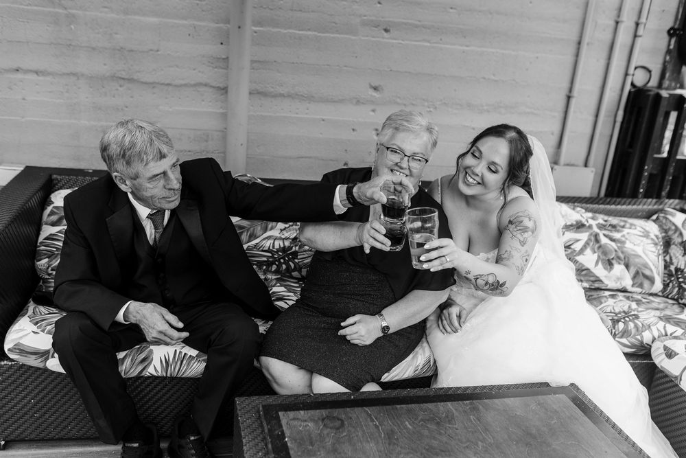 Black and white photo of a bride and two guests toasting with wine glasses at a wedding reception.