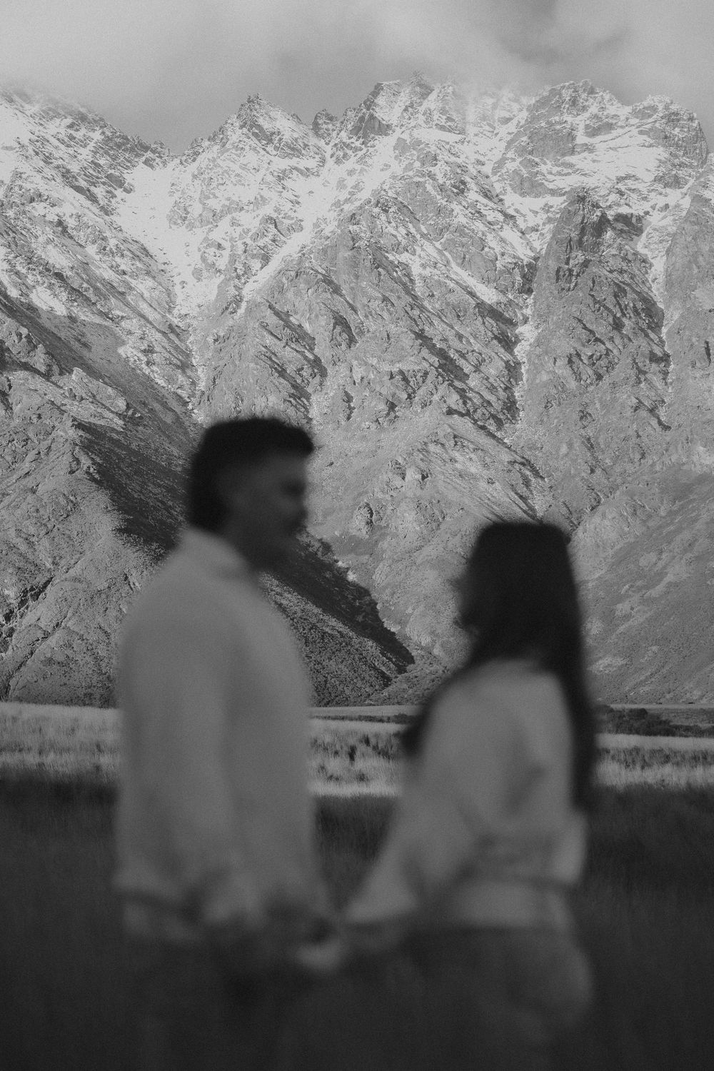 Black and white photo of a couple holding hands with snow-capped mountains in the background.