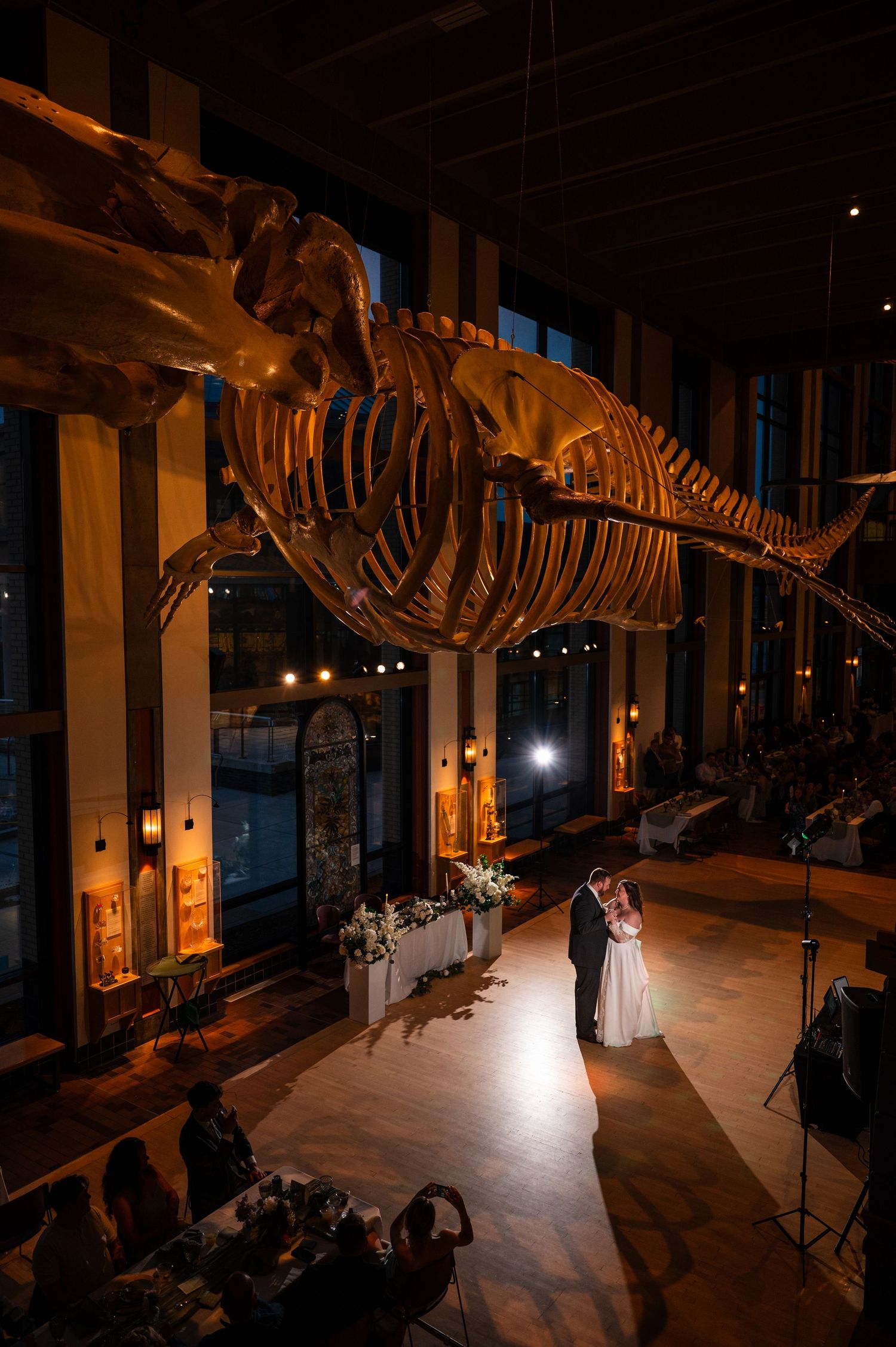 Couple shares first dance beneath a whale skeleton at a candlelit museum wedding reception.