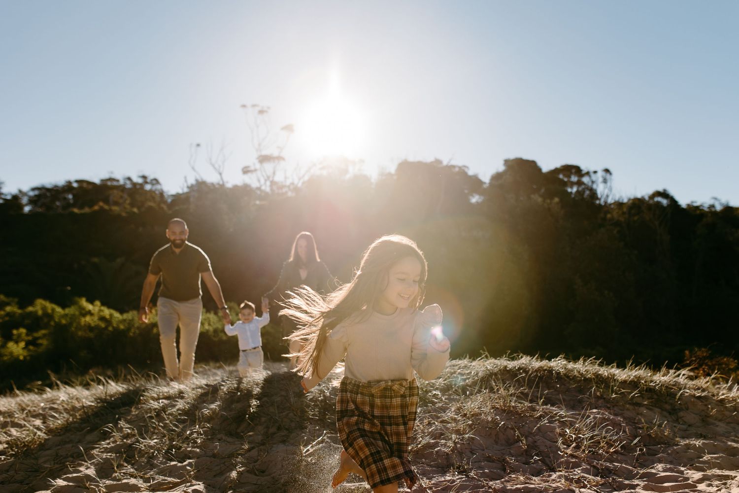 Family enjoying a sunny outdoor walk through golden fields with trees and bright backlit sunlight in the background.
