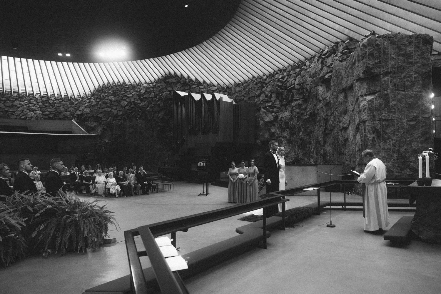 Black and white photo of a church service inside Temppeliaukio Rock Church, Helsinki, with congregation and clergy at altar.