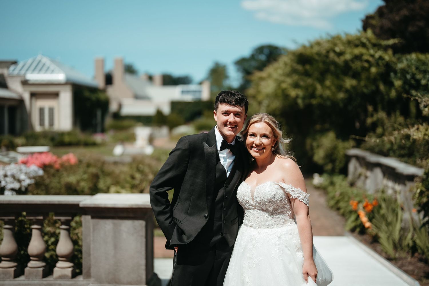 A smiling bride and groom pose together in a lush garden setting on their wedding day.