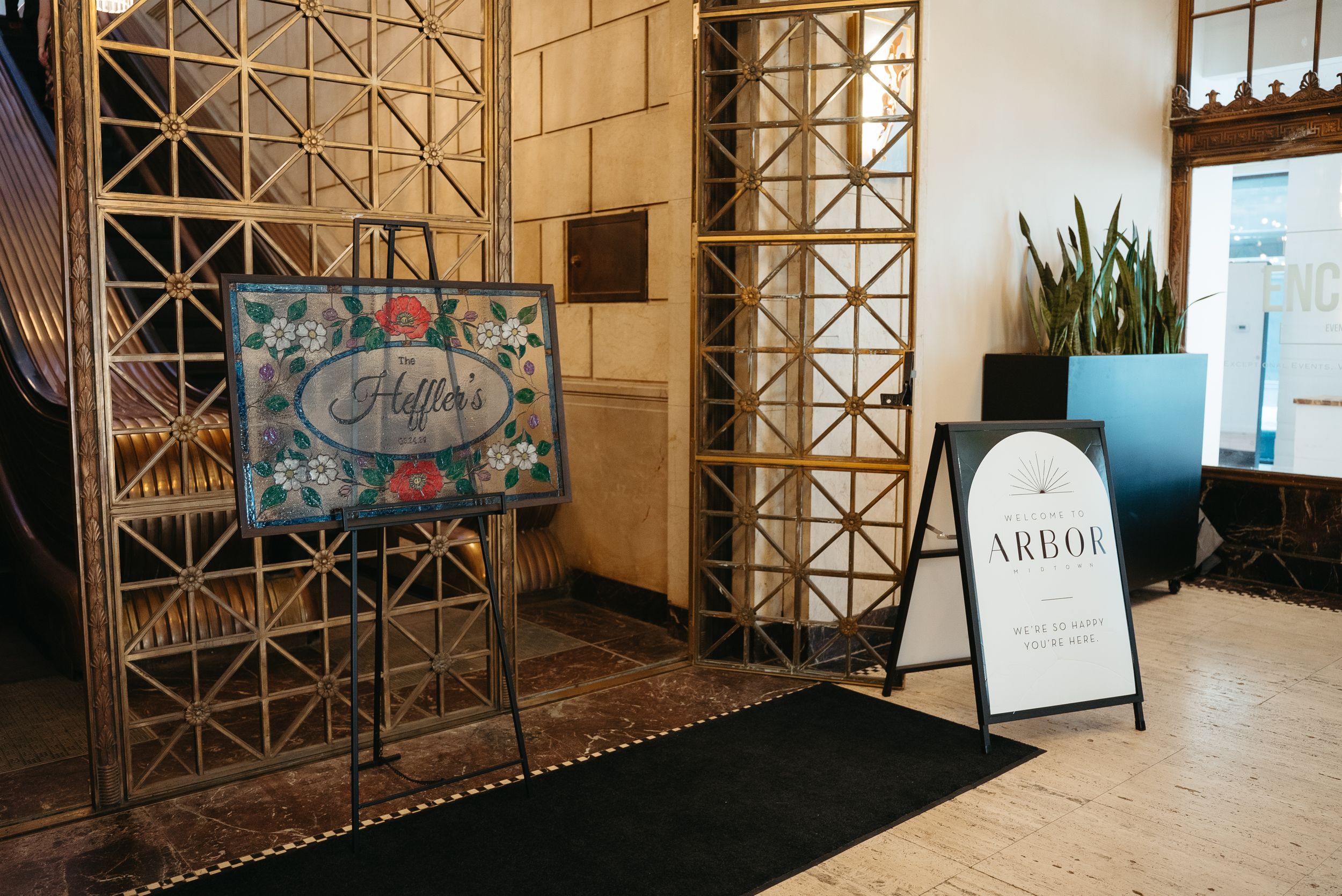 Elegant venue entrance with floral welcome sign and Arbor sandwich board sign on marble floor.