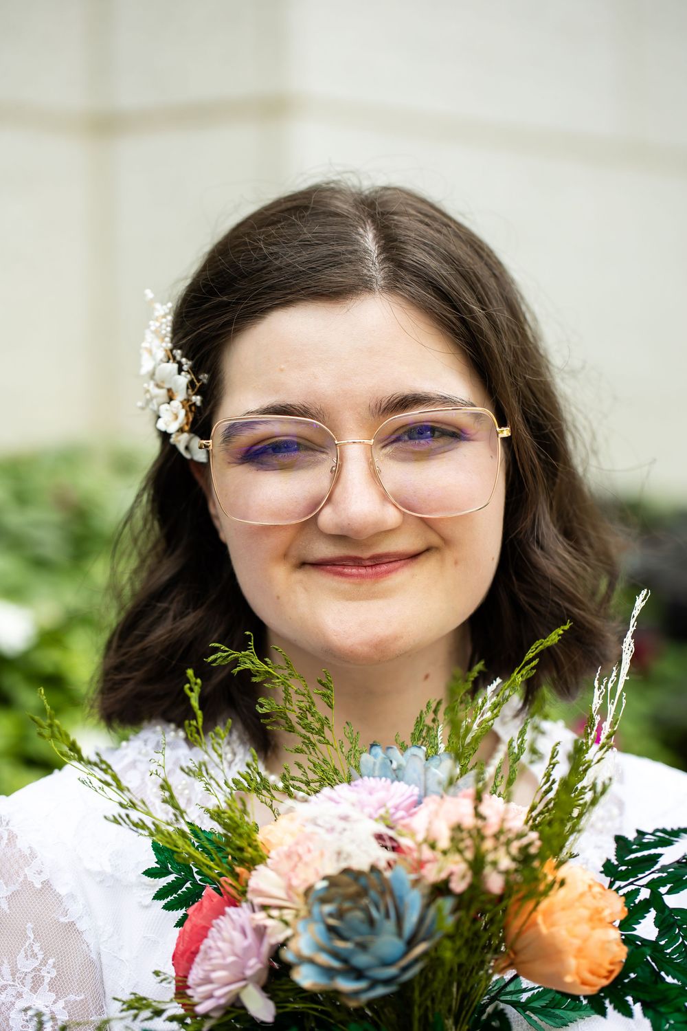 Young woman with glasses and floral hair accessory smiling while holding a colorful bouquet of flowers.