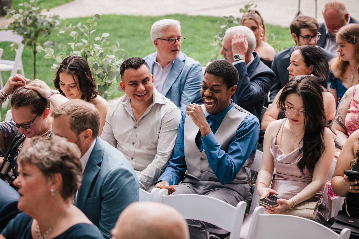 Wedding guests laughing together while seated before the ceremony begins at Searles Castle.