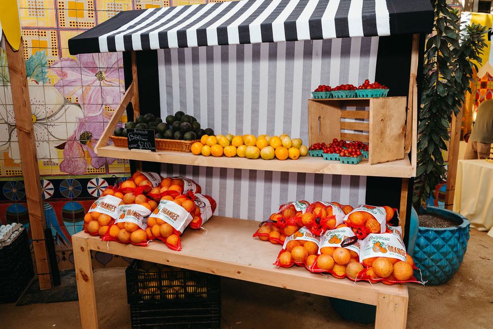 Colorful fruit market stall with oranges, tomatoes, and berries displayed on wooden shelves under striped awning.