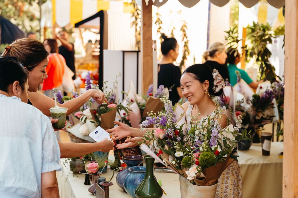 Smiling woman selling fresh flower bouquets at an outdoor market stall to customers.