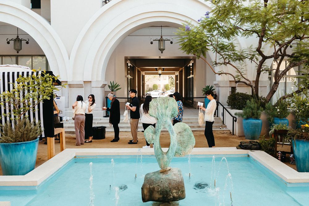 Elegant hotel courtyard with turquoise fountain, bronze mermaid sculpture, and guests exploring lush tropical gardens.