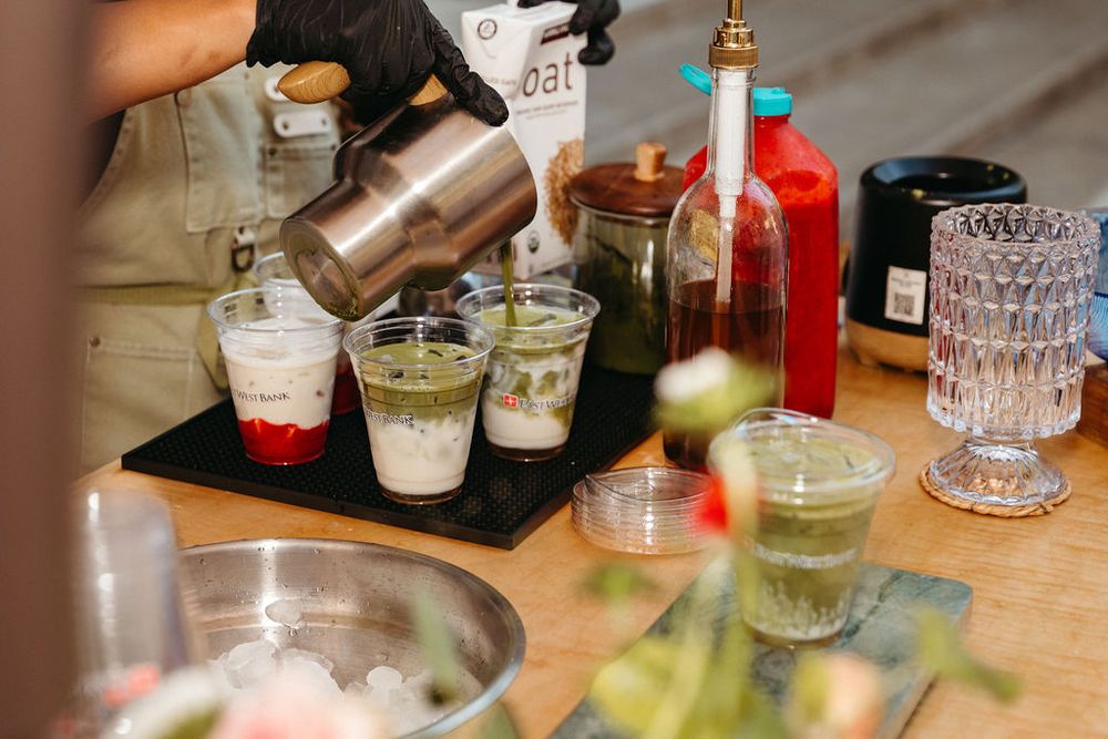 Bartender pouring a cocktail shaker into glasses on a bar counter with bottles and garnishes nearby.