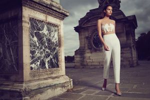 Model in white strapless jumpsuit posing beside an ornate stone monument in Paris.