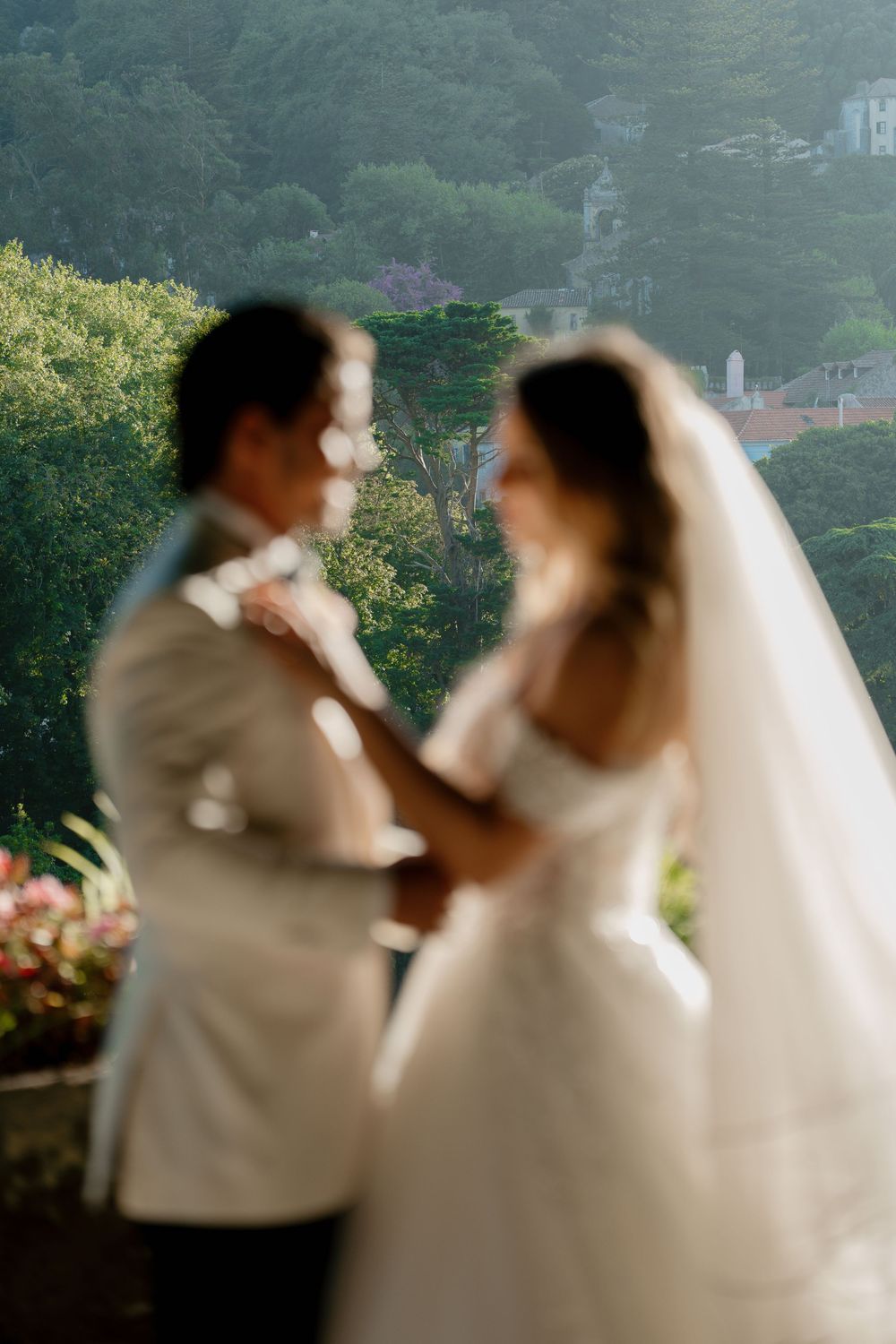 A romantic wedding couple embraces and kisses in a lush garden setting during a beautiful outdoor photoshoot.
