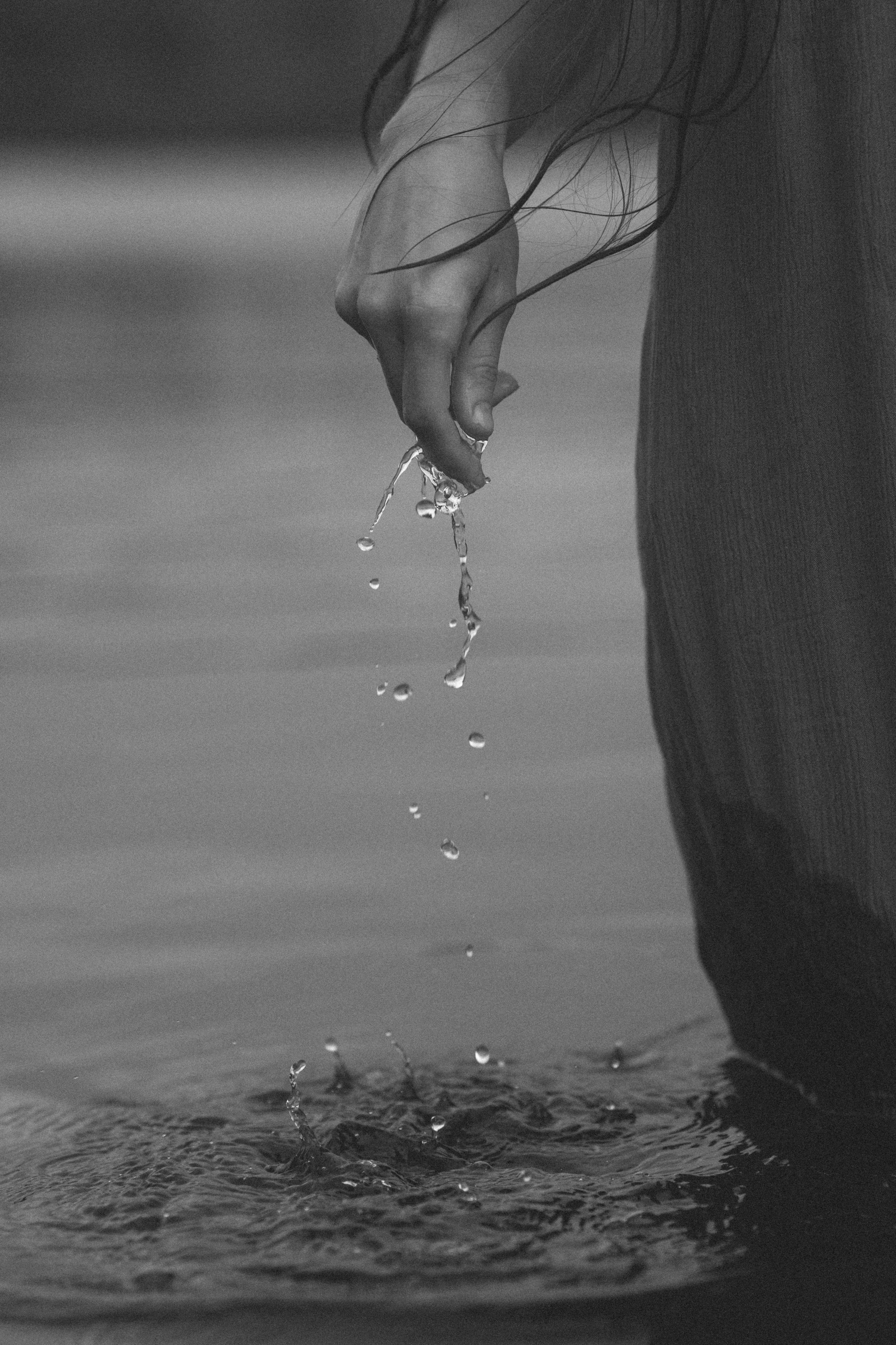 Black and white photo of a hand dripping water droplets into a rippling surface below.