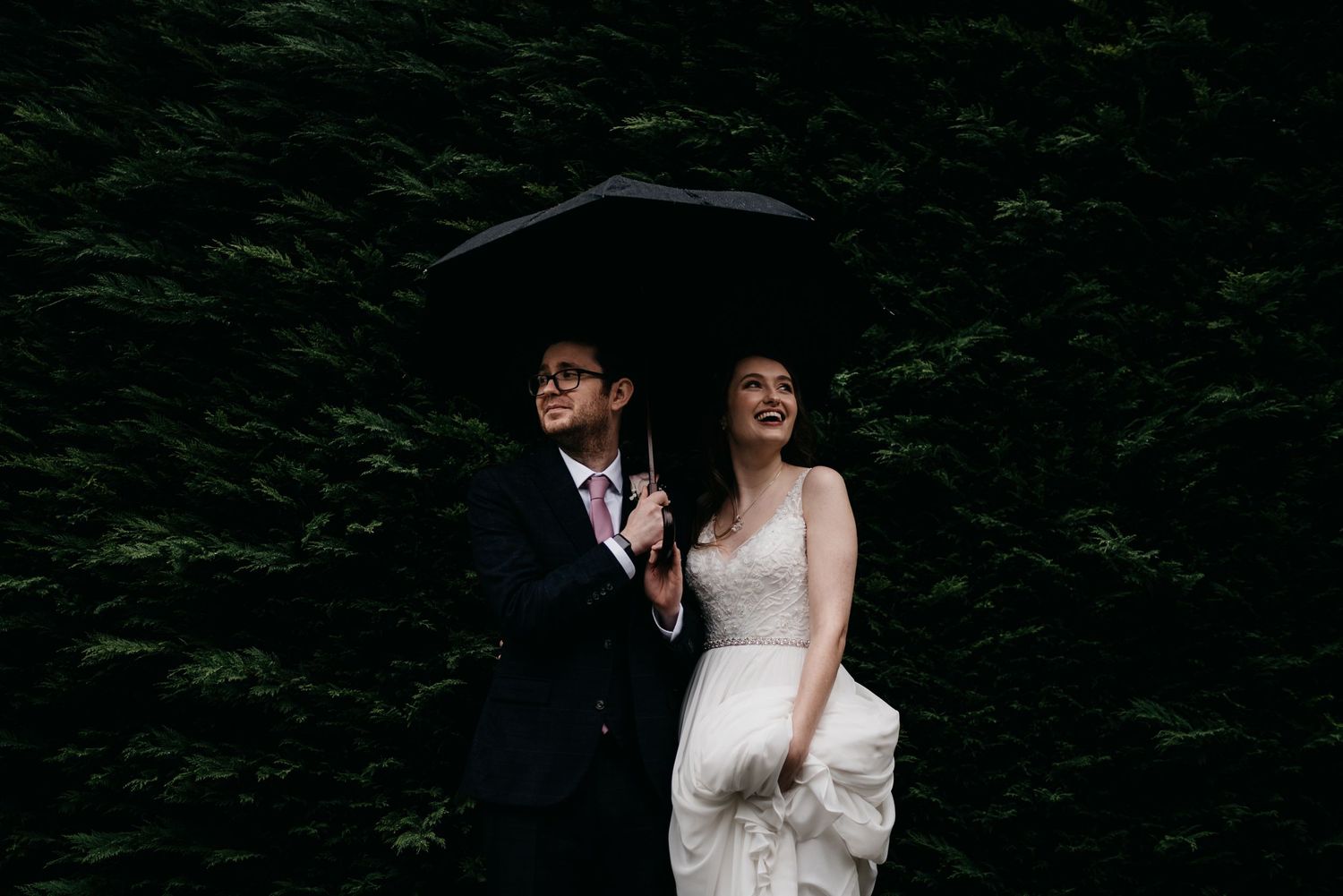 Bride and groom sharing a romantic moment under an umbrella in the rain at their wedding