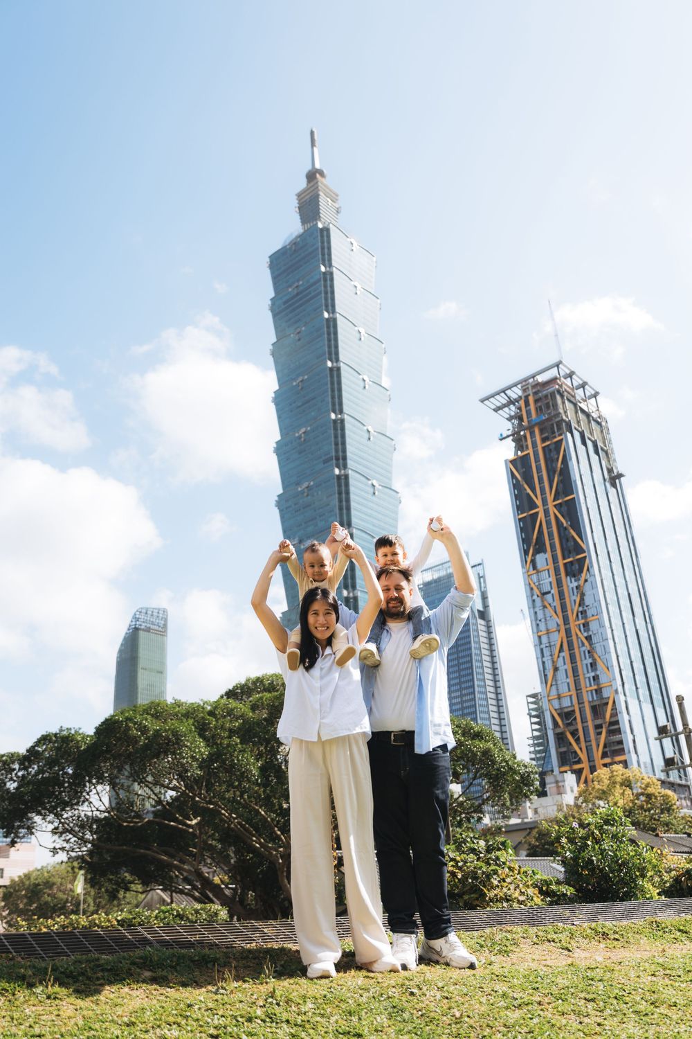 Family posing happily in front of Taipei 101 skyscraper on a sunny day in Taiwan.