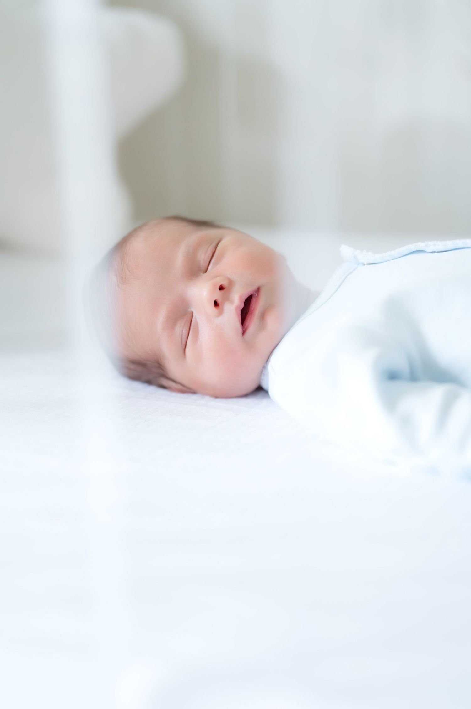 Peaceful newborn baby sleeping soundly in a white crib, dressed in a light blue onesie.