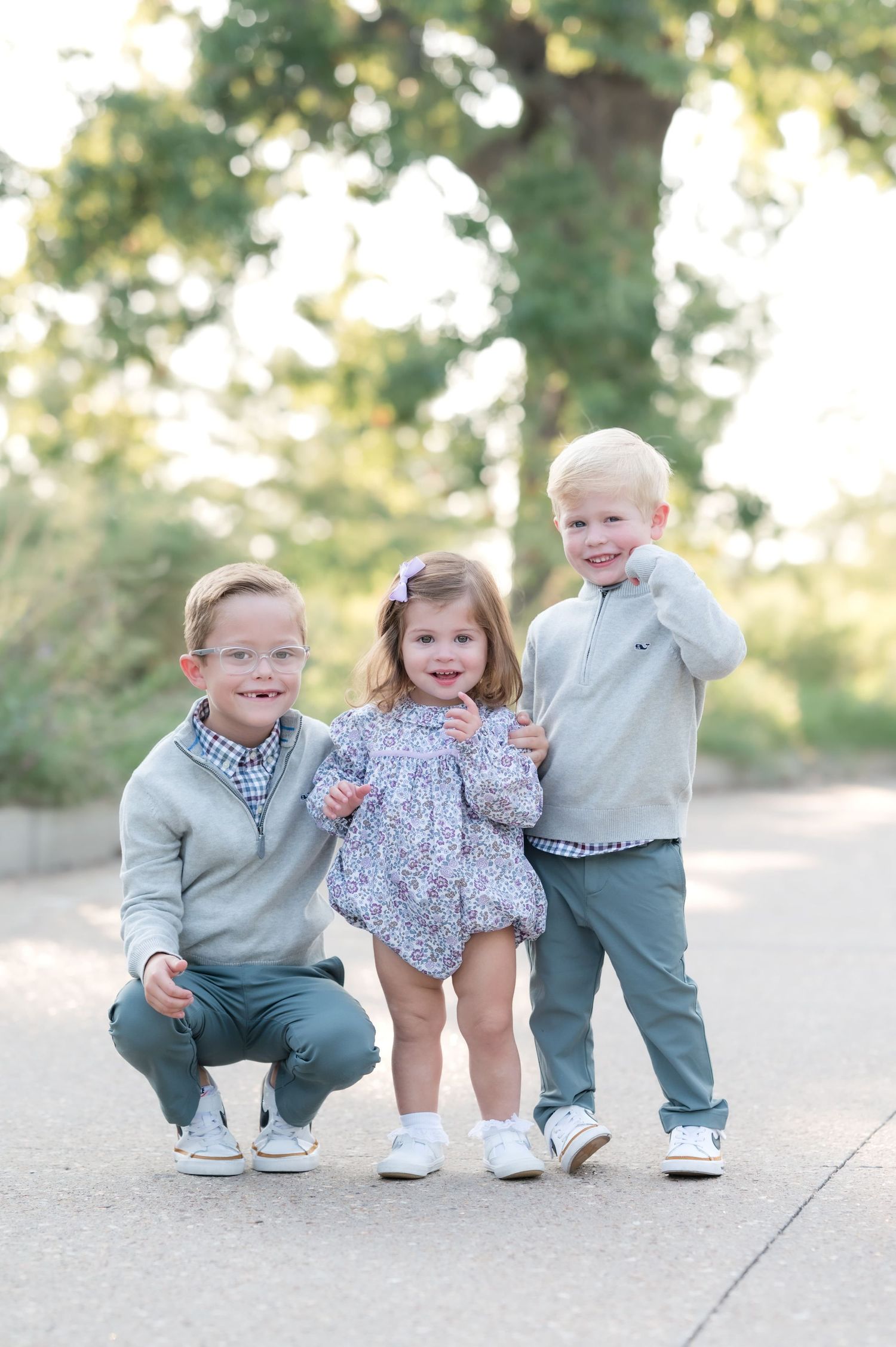 A happy family of five poses outdoors, with parents and three young children sharing warm embraces on a paved path.