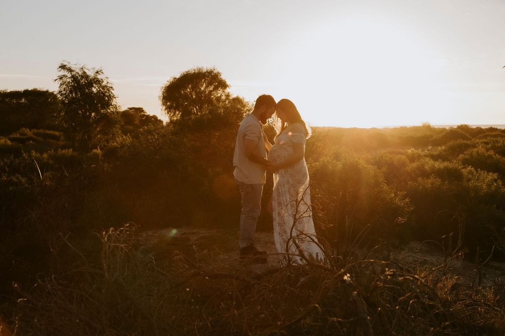 Couple silhouetted against golden sunset light in a natural outdoor setting, sharing an intimate moment.