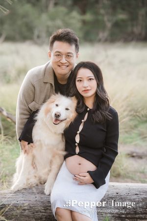 Pregnant woman and man pose with fluffy white dog outdoors in a natural setting for a maternity photo shoot.