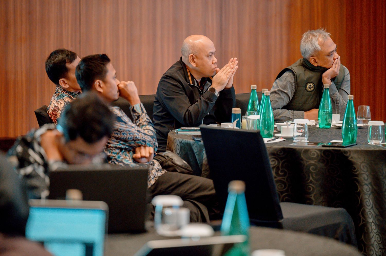 Business professionals attentively listening at a corporate conference meeting with laptops and water bottles on the table.