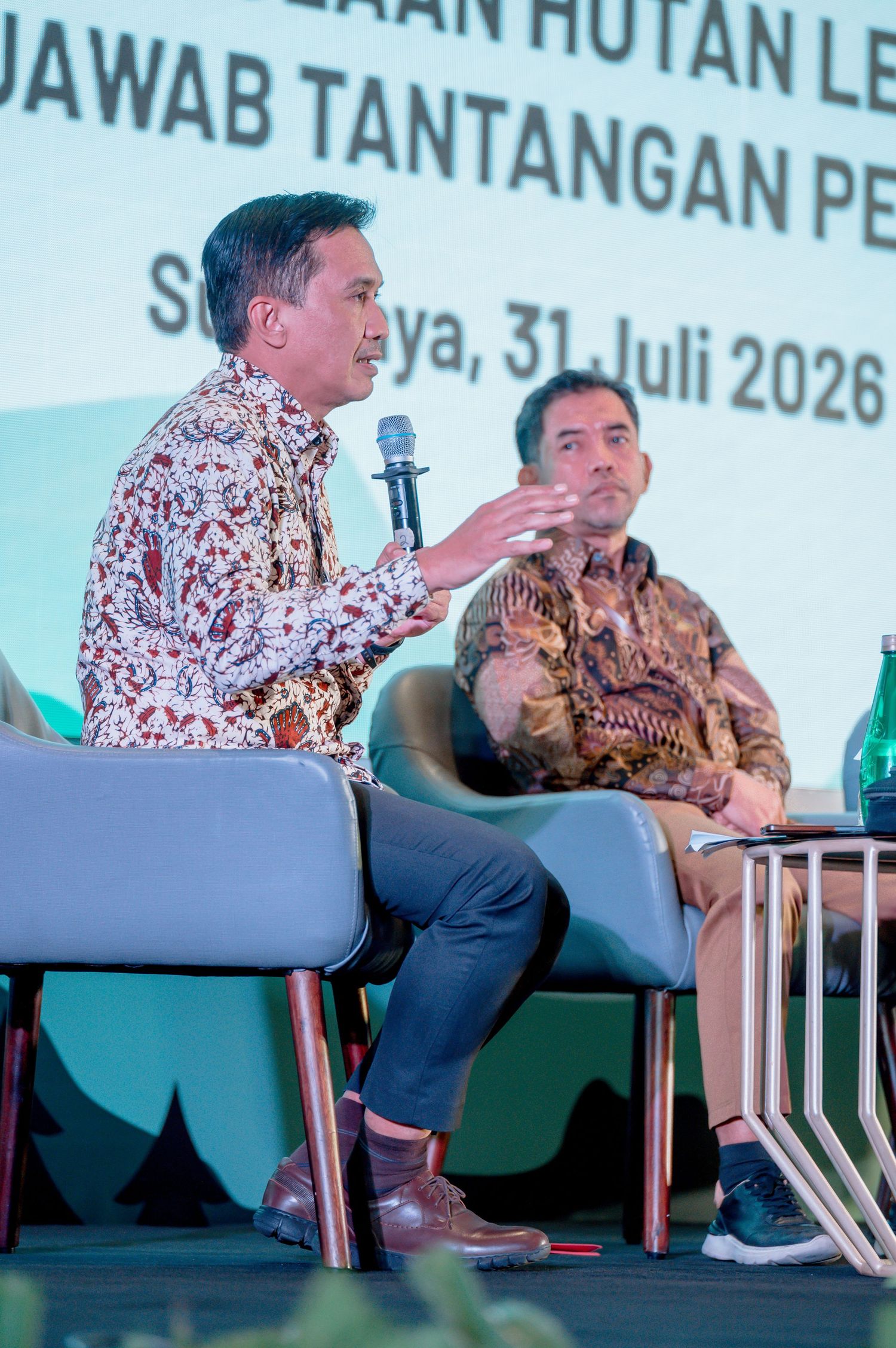 Two men in batik shirts speak at a panel discussion in Surabaya, July 31, 2026, at a forestry management event.
