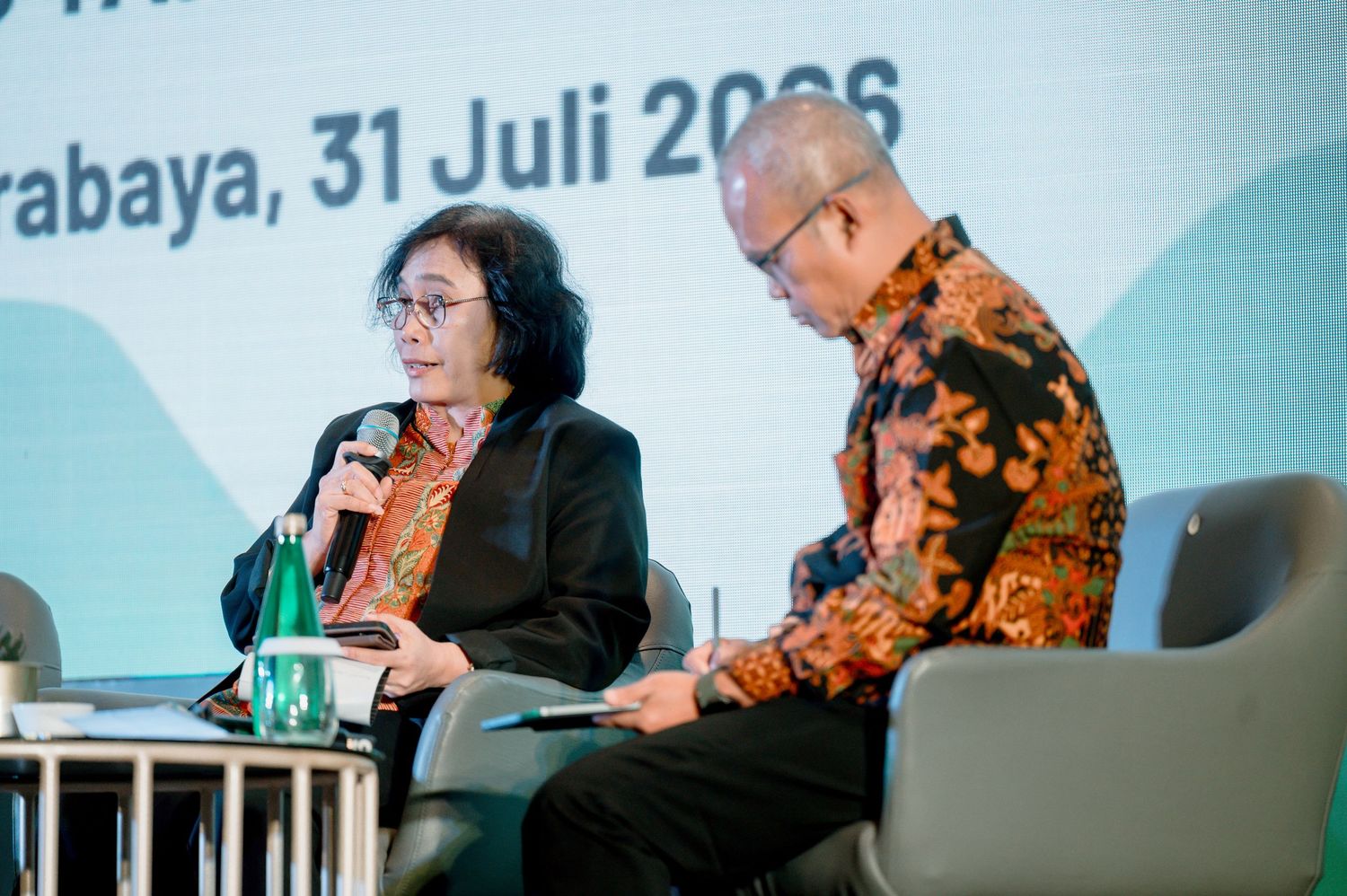 Two professionals speaking at a panel discussion in Surabaya on July 31, 2006, with a woman holding a microphone.