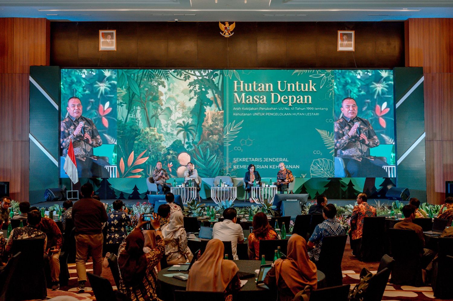 Indonesian forestry conference panel discussion with speakers on stage beneath a green forest-themed backdrop reading Hutan Untuk Masa Depan