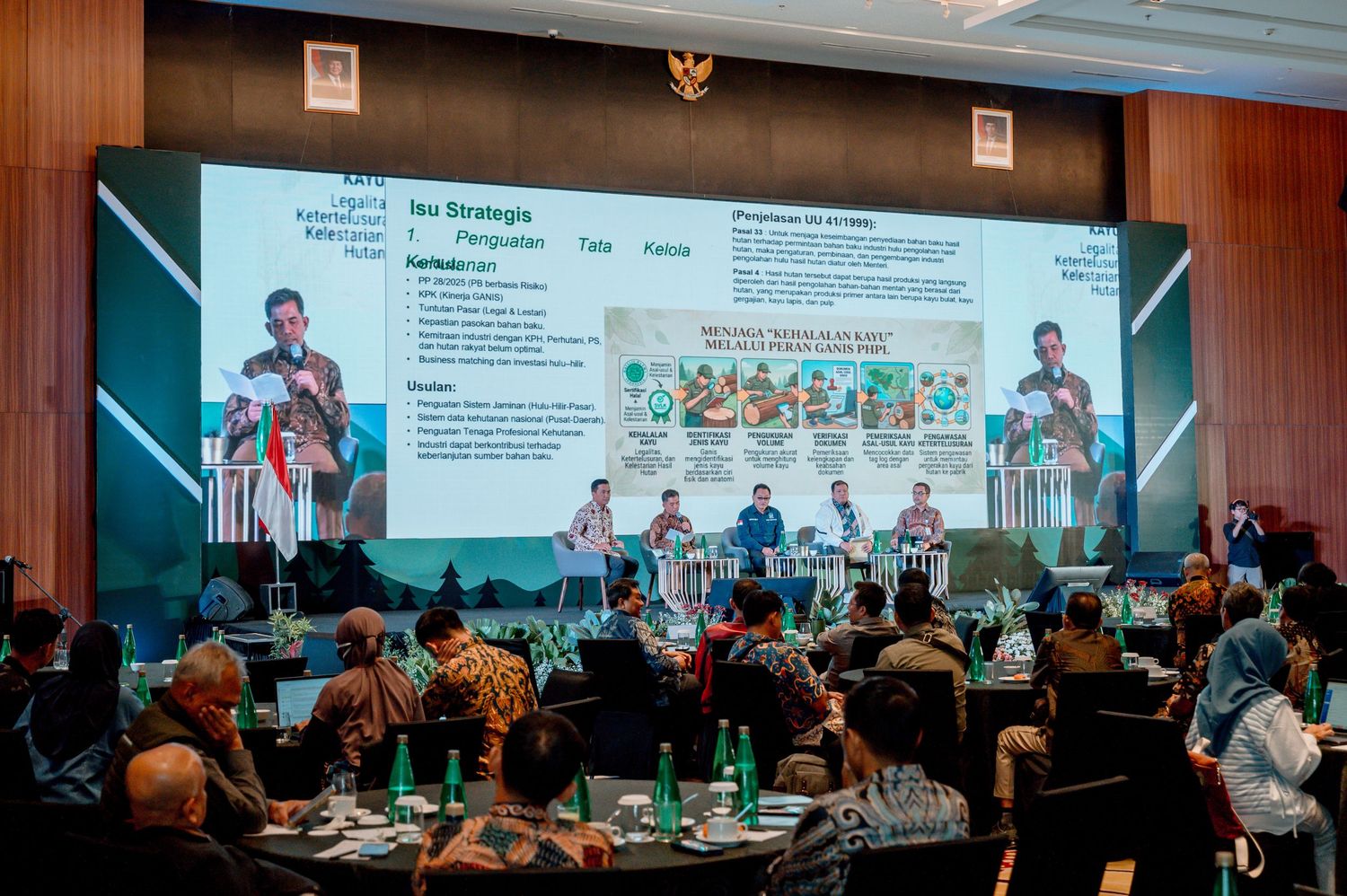 Conference panel discussion with speakers on stage before a large presentation screen displaying strategy slides in Indonesia.